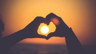 hands form heart around setting sun