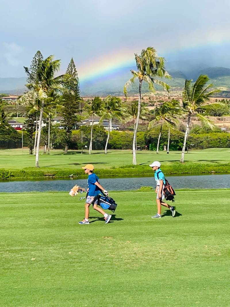 young boys walking the golf course in hawaii under rainbow