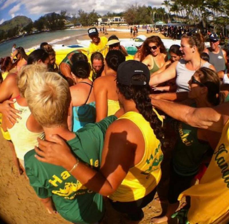 people huddles together on the beach for outrigger canoe race