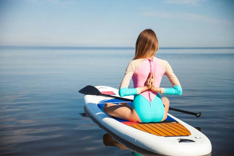women sitting on a paddleboard with hands in prayer behind her back