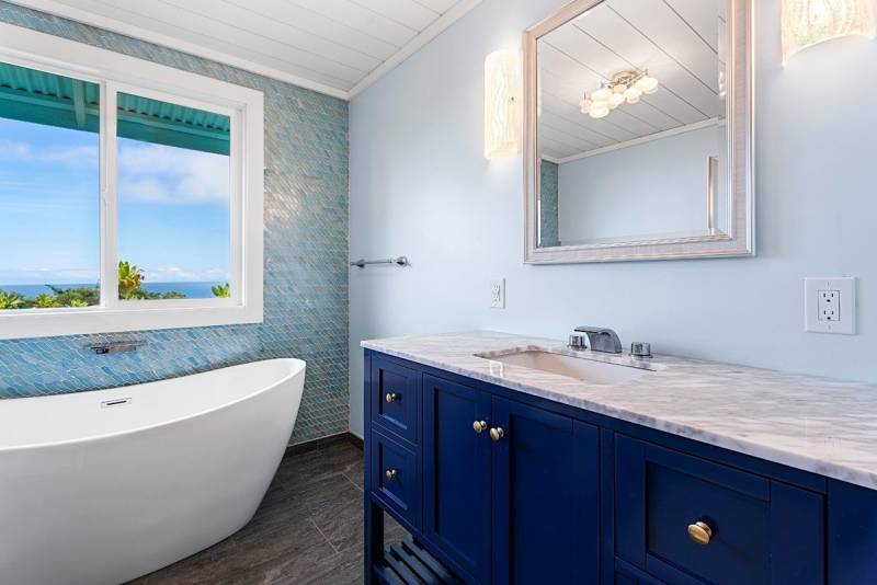 ocean view bathroom with soaking tub, light blue tiled while and navy blue vanity 