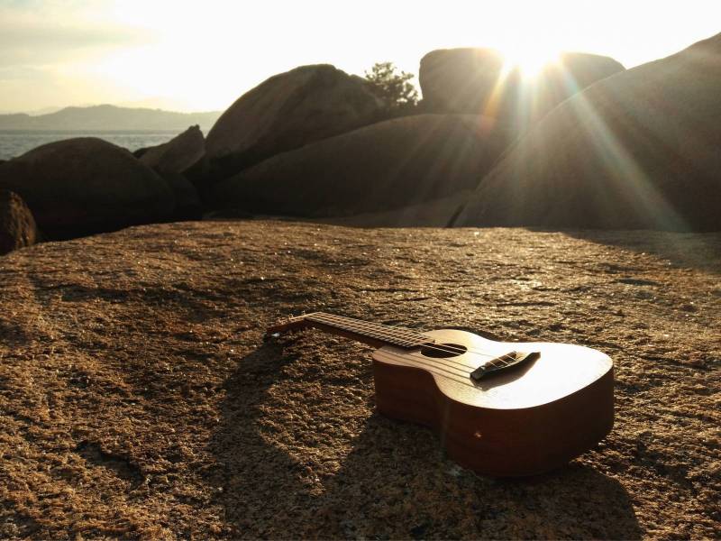 guitar on the ground with sun rays peeking over a rock