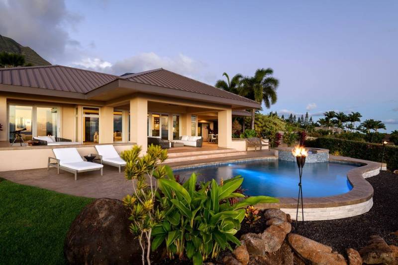 back of maui home with lounge chairs, swimming pool, and torches lit