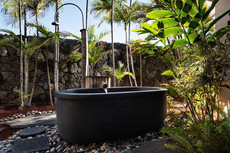 outdoor bathtub surrounded by stone walls and tropical plants