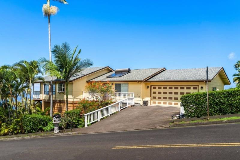 street passes in front of creamy yellow big island home for sale with peek of ocean in background