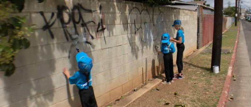 kids painting over graffiti on block wall