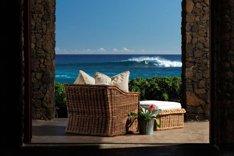 view of surfer on wave through rock pillars at oceanfront home on kauai