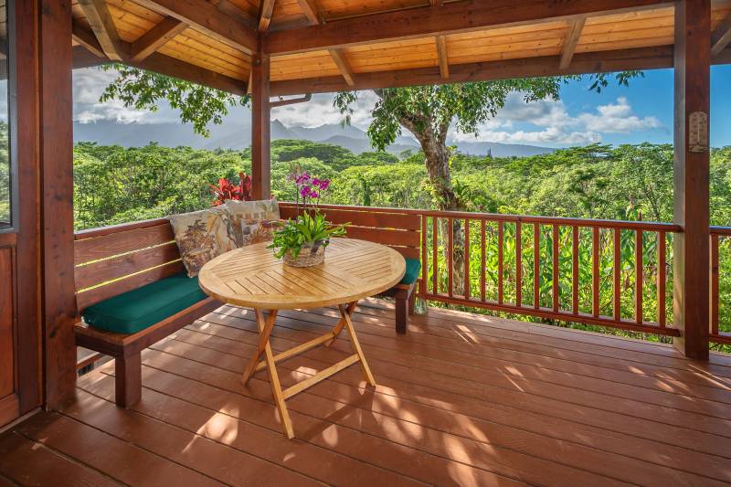 covered lanai with table and benches for seating, view looks out to green valley and mountain views