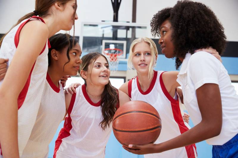 4 women basketball players and a coach in a huddle