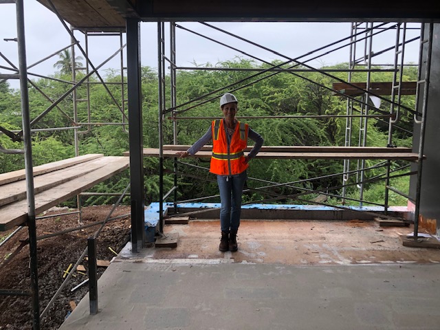 woman poses in orange vest below scaffolding on maui construction site