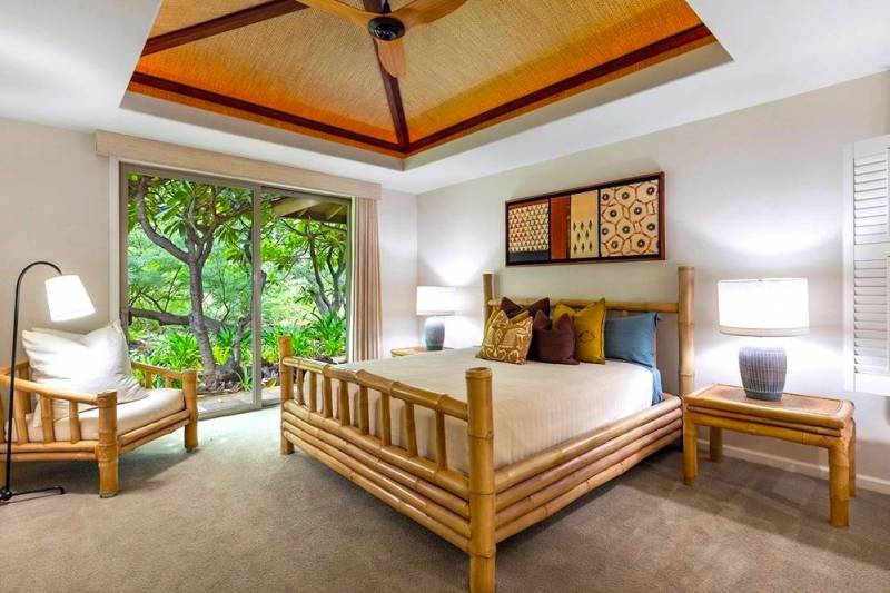 hawaii island condo bedroom with wood framed furniture and large window to green landscaping outside