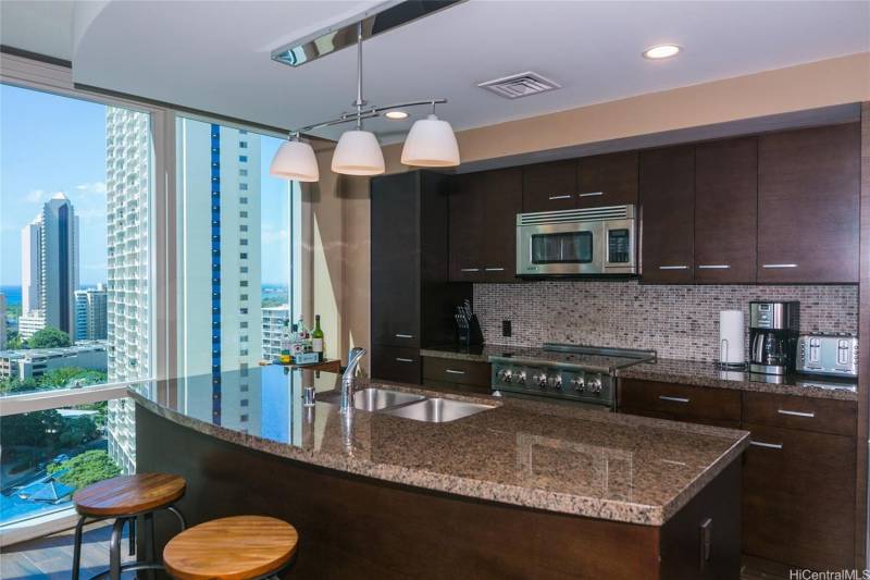 stone countertops and dark wood cabinets in condo kitchen with honolulu city and ocean views out the window