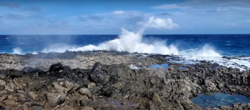 waves crash on black rocks on oahu