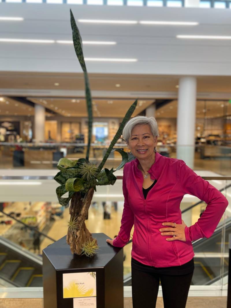 woman poses next to plant arrangement