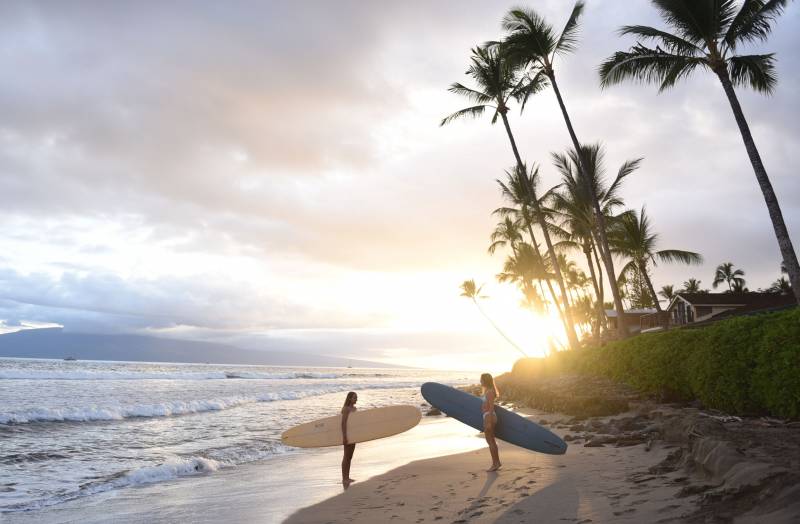 two people holding surfboards on west maui beach 