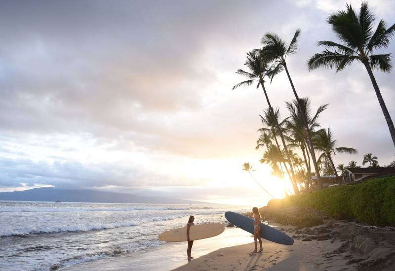 two women holding surfboards on puamana maui beach