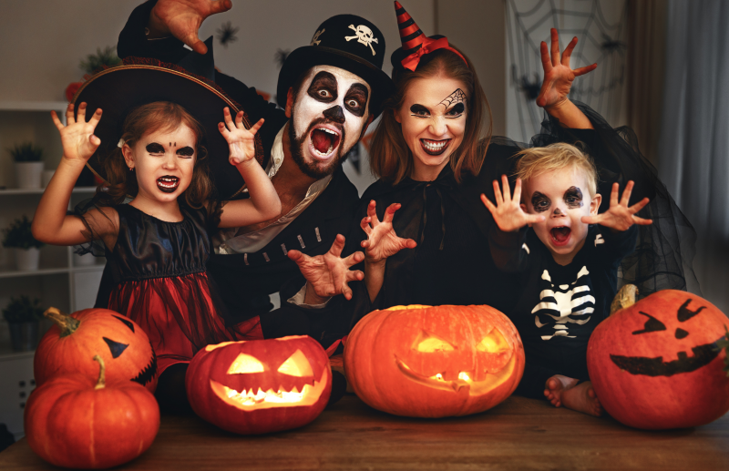 mom. dad, and two children dressed up for halloween posed behind jack o lanterns
