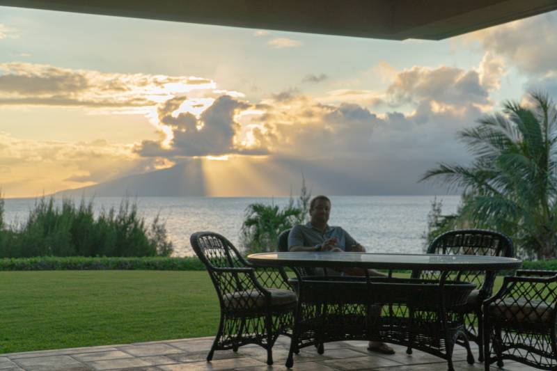 man sits at table in front of maui sunset over the ocean