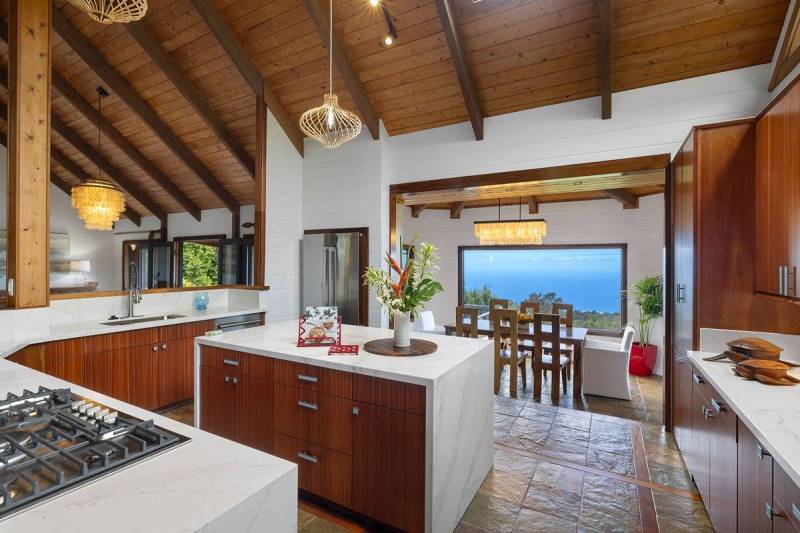 modern kitchen with warm wood cabinets and white stone countertop overlooks ocean views