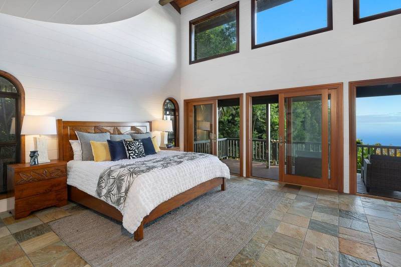 bed and nightstands furnish spacious bedroom with high ceilings and glass doors to lanai