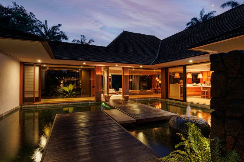 pathway over water to luxurious kauai home lit with warm light at dusk