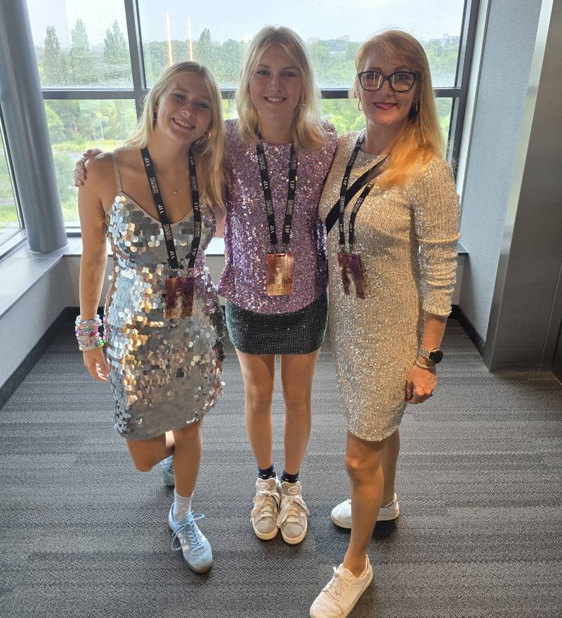 mom and two teenage daughters pose in front of window