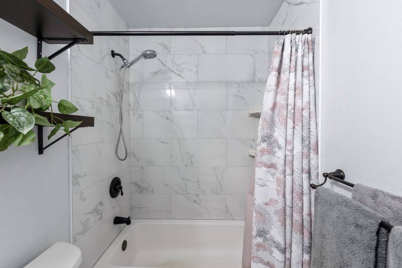 bath tub shower combo with marble tile walls and black fixtures