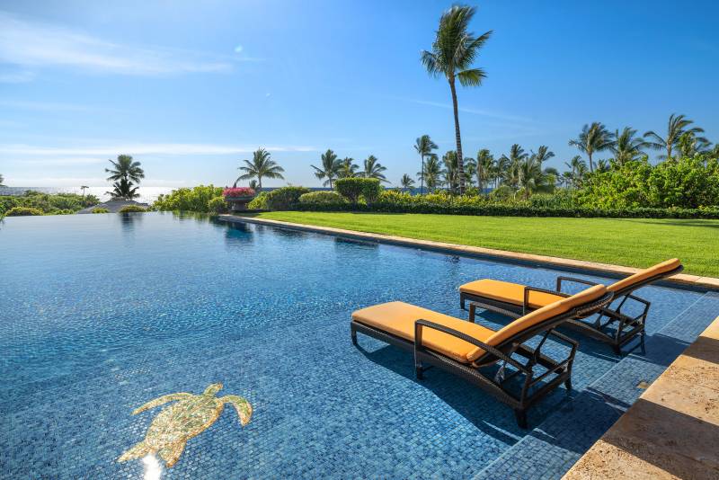 yellow lounge chairs sit in expansive pool at kukio estate on big island hawaii