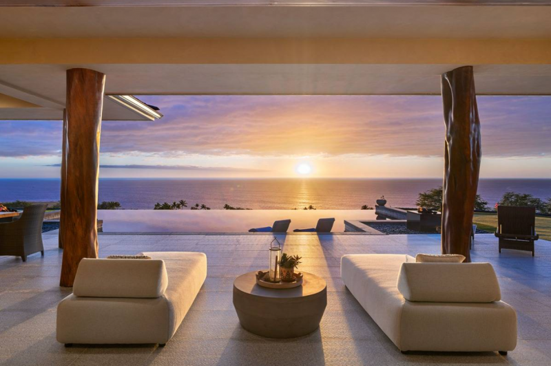 chairs on patio look at the sunset from over the pool and ocean in the distance