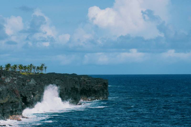 wave crashes on black rocky cliff on big island hawaii