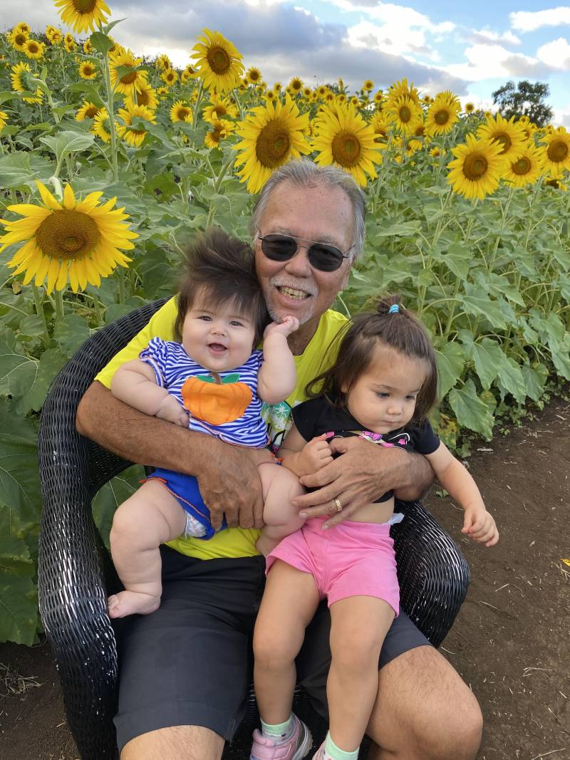 grandpa holding two babies in front of field of sunflowers