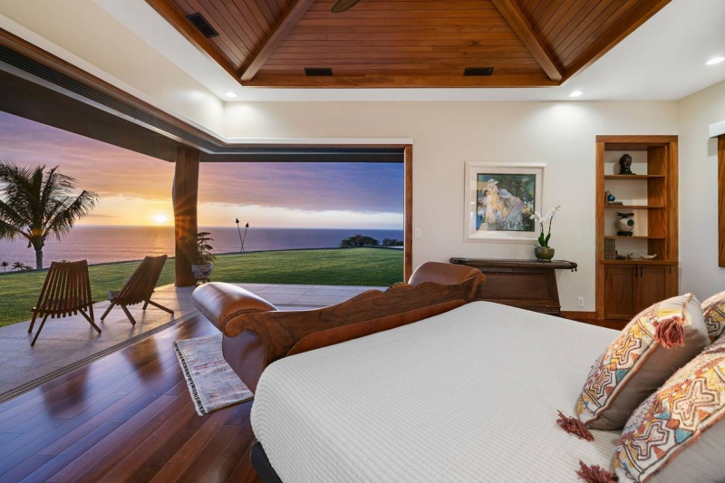 bedroom with large open sliding doors let in sunset glow over the ocean in hawaii