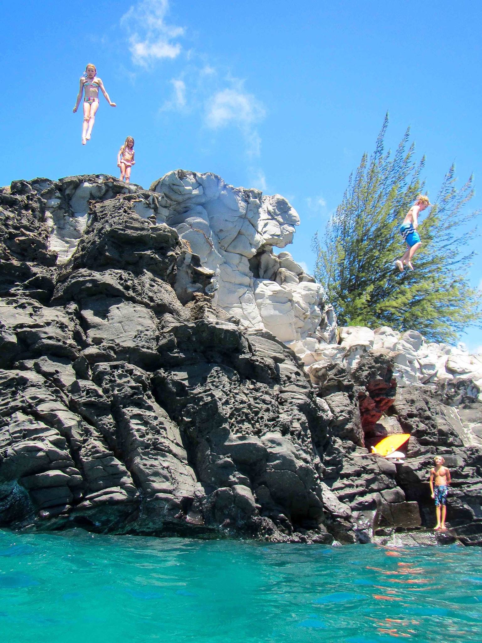 Kids jumping off rocks into crystal clear Maui ocean