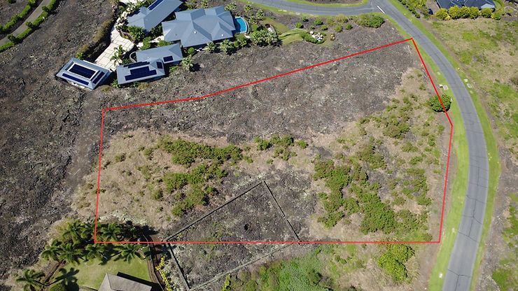 Aerial view of Hokulia Big island plot of land outlined in red, adjacent to a house with solar panels and a road. Green vegetation and barren soil visible.