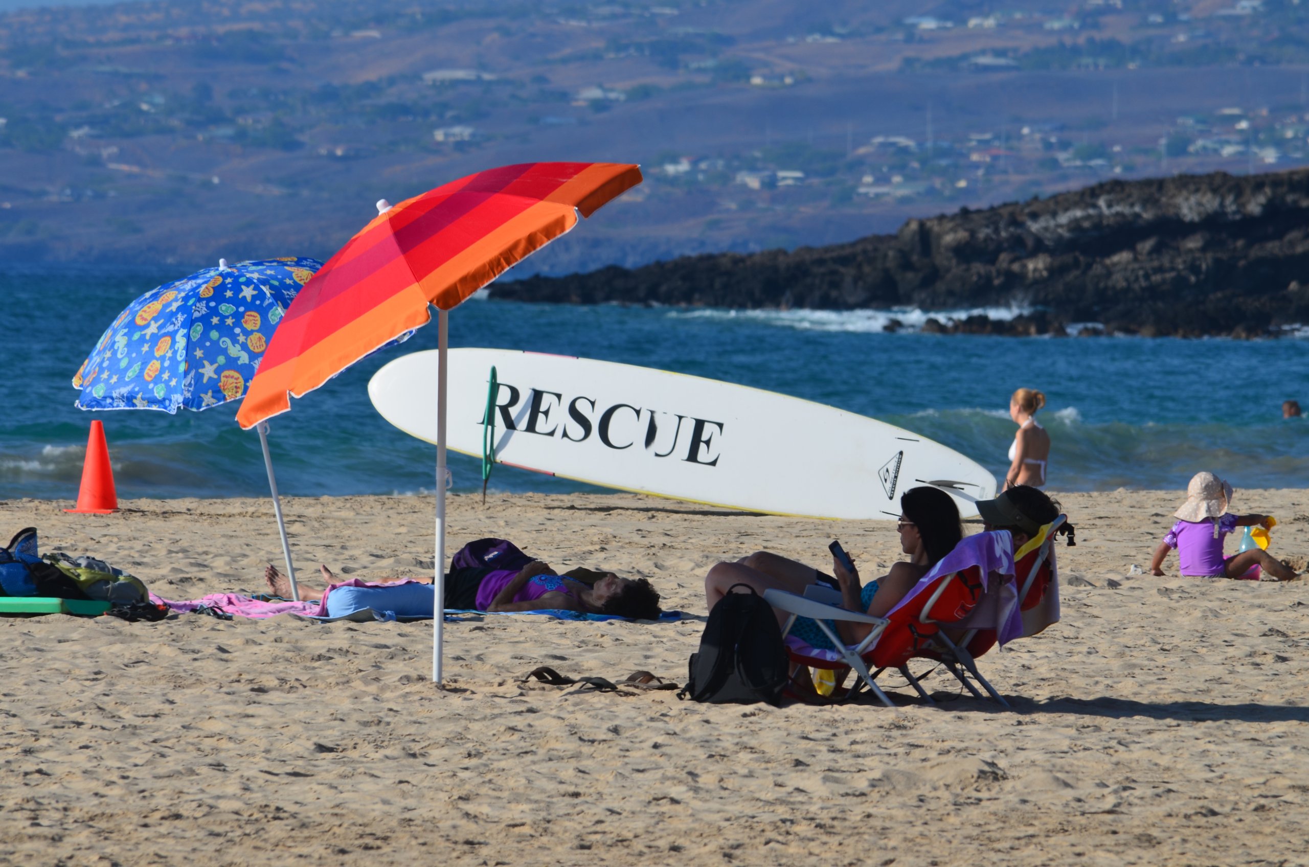 Beach scene with umbrellas and rescue surfboard.