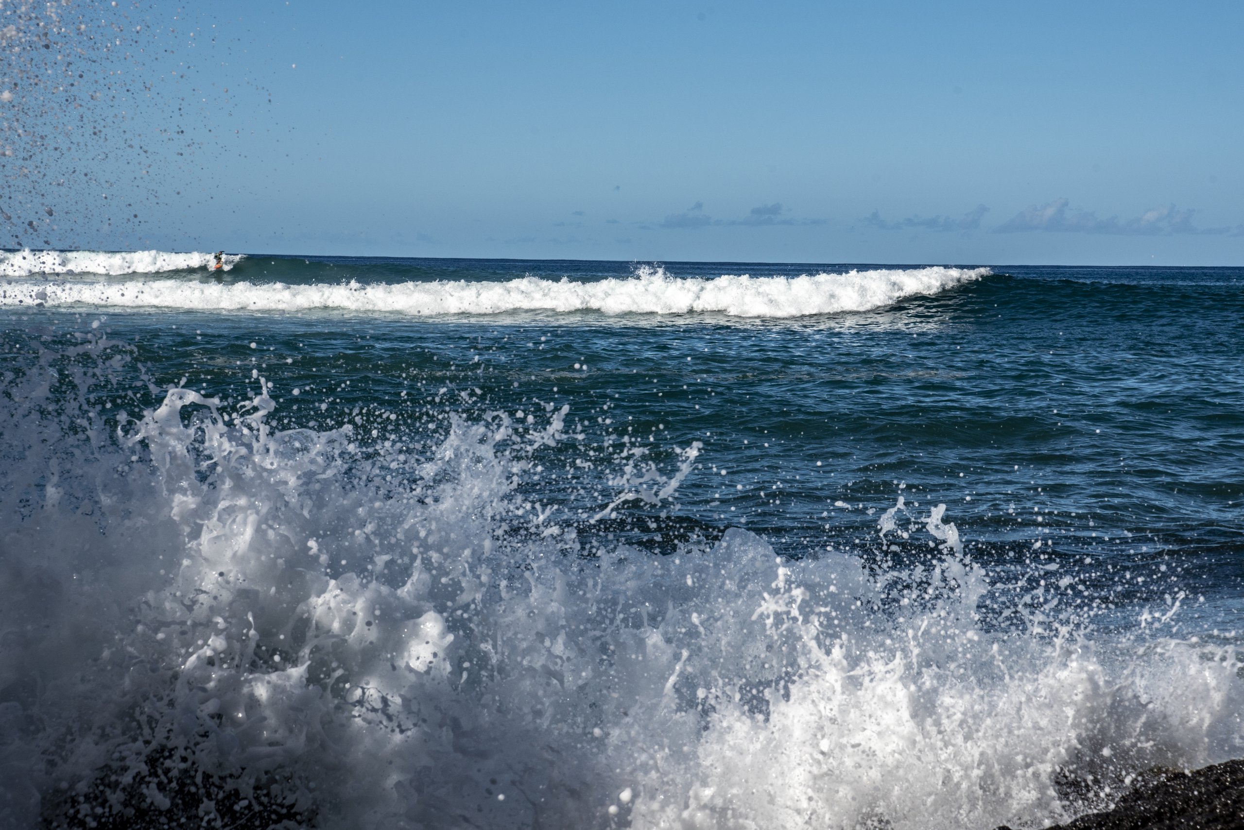 Ocean waves crash against rocks under a clear blue sky.