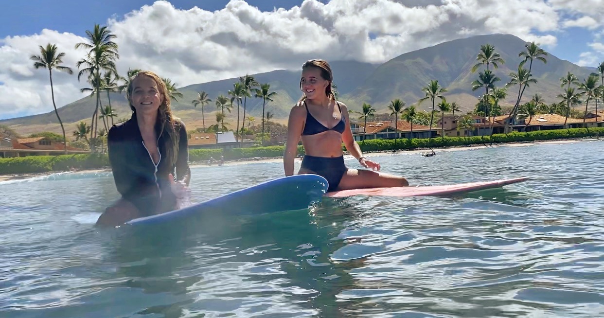Anna severson and daughter on surfboard in the ocean in front of Puamana Maui