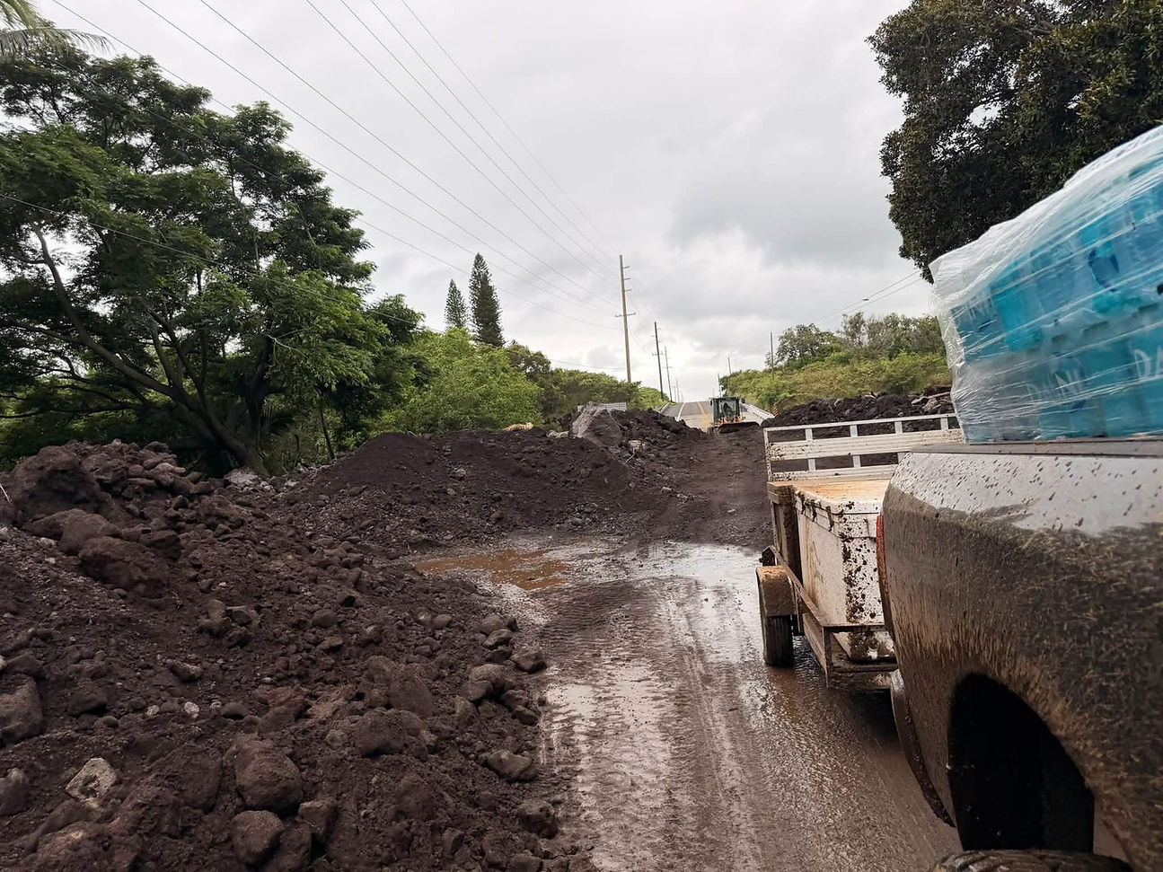 A muddy landslide washes out a road beside a raging river, with a few people standing near broken guardrails and debris.